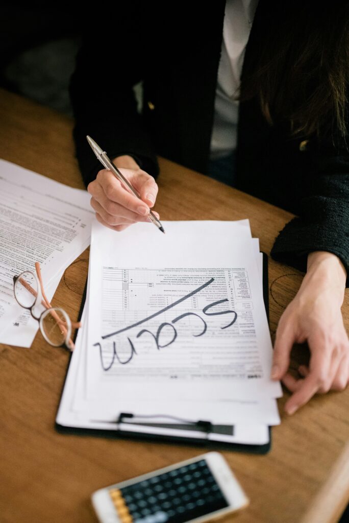 A person marking documents as scam with glasses and a calculator nearby.